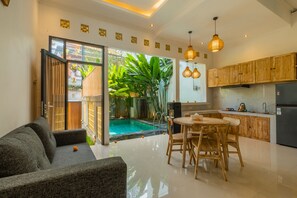 Una cocina moderna con armarios de madera, un comedor con mesa y sillas, y un ventanal que da a una zona de piscina con plantas.