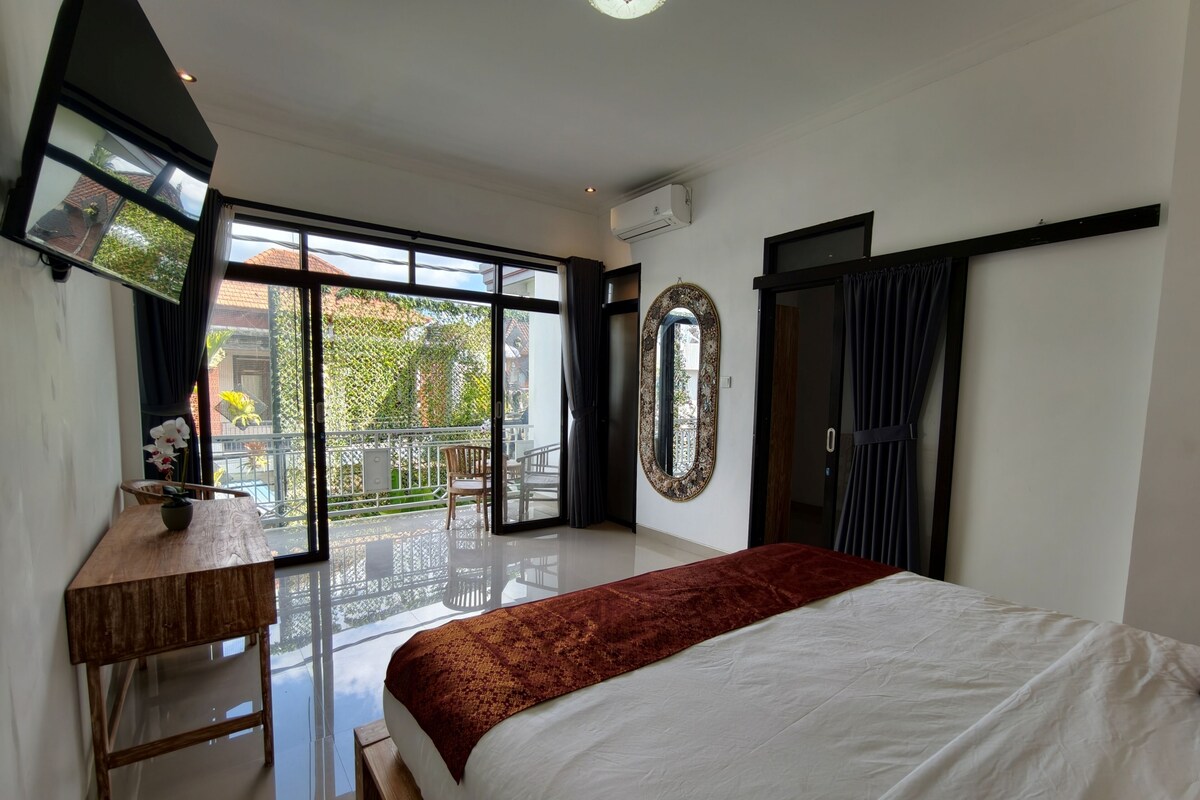 Un dormitorio con cama, escritorio, espejo y balcón con vistas.