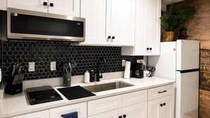 Eine moderne Küche mit weißen Schränken, einer schwarzen Spritzschutzwand, einer Edelstahl-Dunstabzugshaube, einer eingebauten Mikrowelle, einem Spülbecken und einem Kühlschrank.