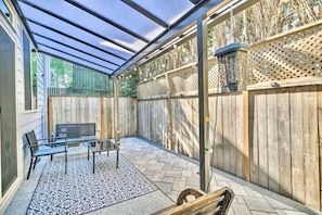 Un patio cubierto con techo de vidrio, cerca de madera, banco de metal y alfombra estampada.