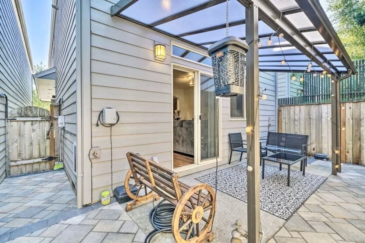 A covered patio area with a wooden bench, a table, and a hanging light fixture.