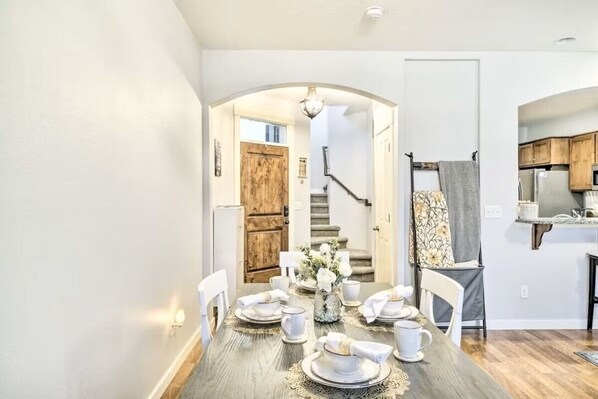 A dining area with a wooden table set for four, a staircase, and a kitchen visible in the background.