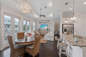 A spacious living area with a dining table, wicker chairs, and a large window overlooking a balcony. - Luxury Prominence Retreat | Bikes, Resort Pool & Walk to The Big Chill (Watersound)