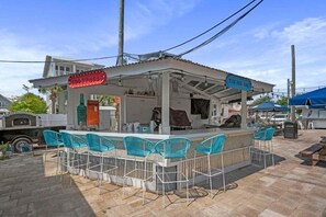 Eine Bar im Freien mit einer Theke, Barhocker und einem Schild mit der Aufschrift 'COCA COLA'.