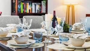 A dining table set with glassware, plates, and bowls, with a candle and a bottle in the background.