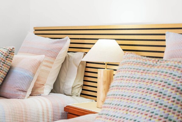 A bed with a wooden headboard, a bedside lamp, and multiple pillows.