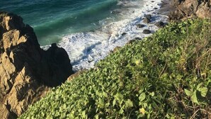 A coastal landscape with a rocky shoreline, a sandy beach, and a clear blue sky.