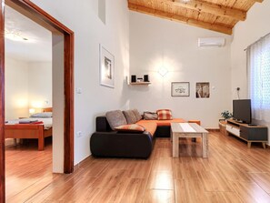 Un saló modern amb un sofà, una taula de centre i un televisor. Té un sostre de fusta i una porta que condueix a una altra habitació.