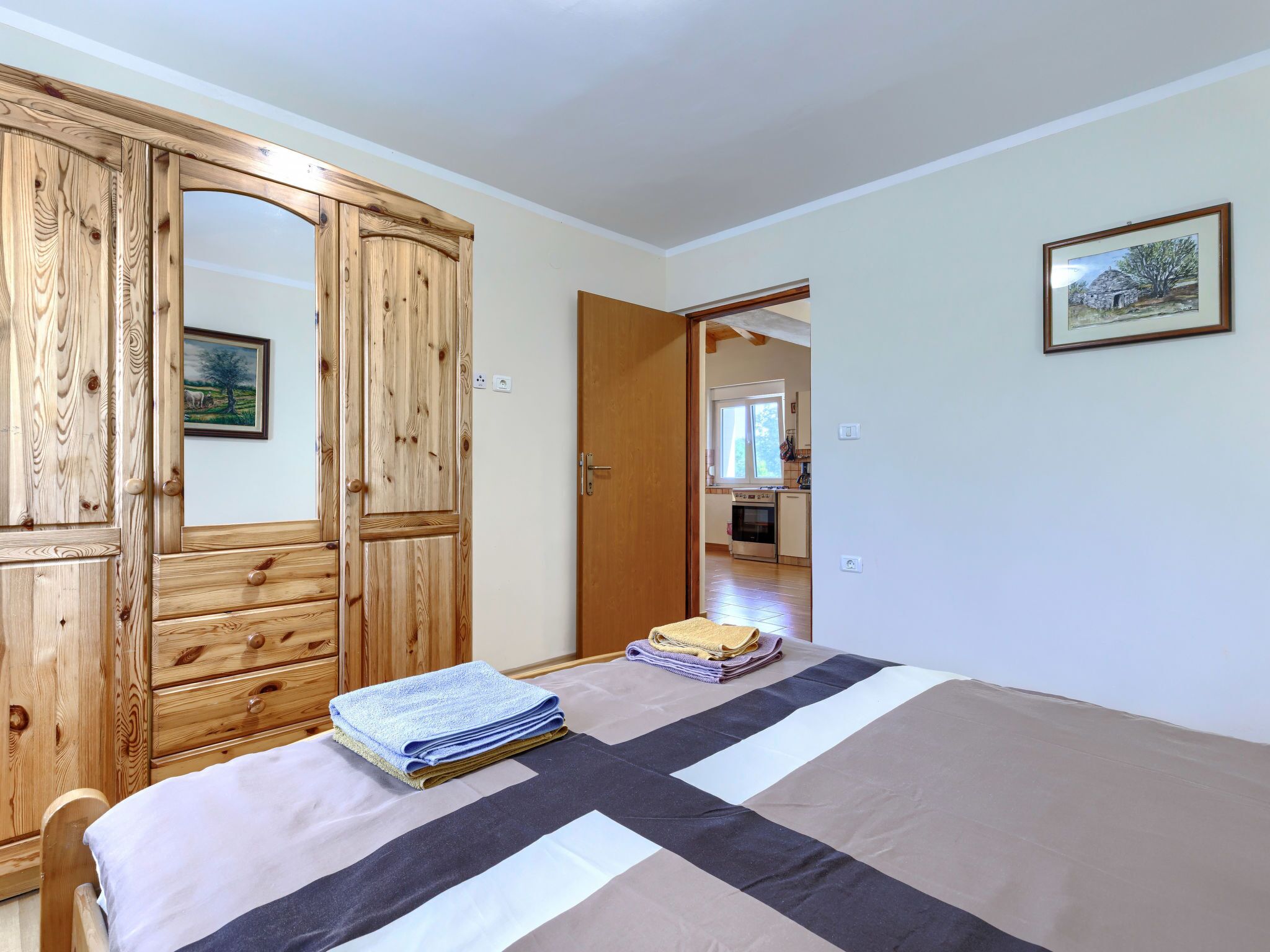 Een slaapkamer met een bed, een houten garderobe en een schilderij aan de muur.
