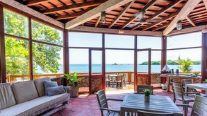 A covered outdoor seating area with a view of the sea, wooden furniture, and potted plants. - Raices del rosario  (Rosario Islands)