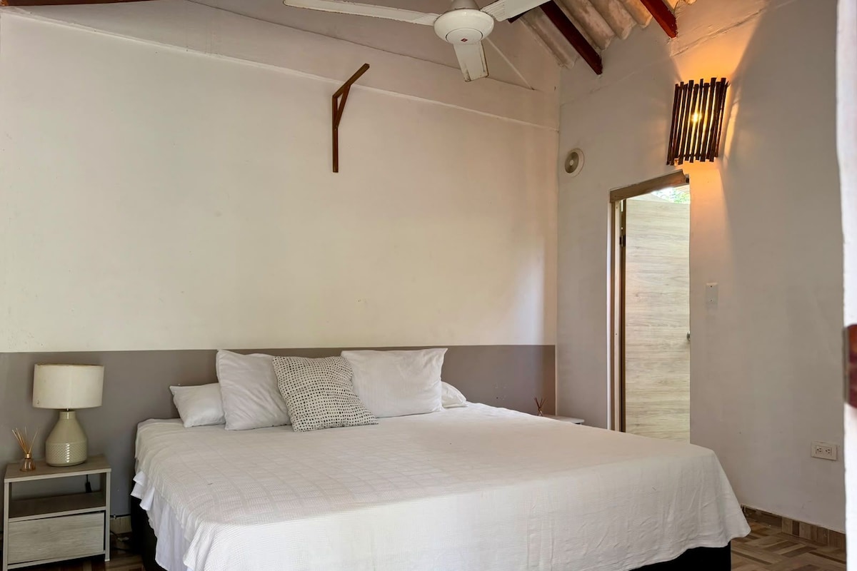 Quarto com cama, mesa de cabeceira, luminária e ventilador de teto.