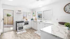 A modern kitchen with white cabinetry, a marble countertop, and a black stove. - Unit 1 (Anna) Beachside Mackay (Slade Point, Mackay)