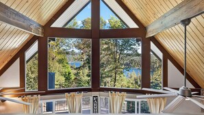 A room with a sloped ceiling, large windows, and a view of a forest and lake. - North Bay Chalet by Avantstay A-frame + Game Room Deck Dining + Firepit + Lake Views Near Dining (Lake Arrowhead)