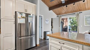 A kitchen with white cabinetry, stainless steel appliances, a granite countertop, and a view to an outdoor patio. - North Bay Chalet by Avantstay A-frame + Game Room Deck Dining + Firepit + Lake Views Near Dining (Lake Arrowhead)