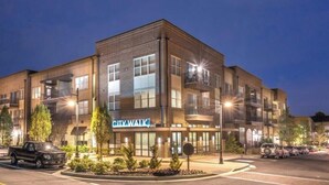 Un edificio de varios pisos con un letrero 'CITY WALK', fachada de ladrillo, múltiples balcones y un estacionamiento con automóviles.