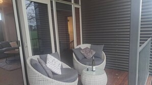 Two wicker lounge chairs with cushions on a wooden deck, a glass door leading to an interior space, and a metal railing. - Spacious 5 Bedroom House in Ngāhinapōuri Family Retreat (Ngahinapouri)