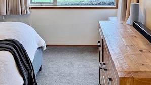 A bedroom with a large window, a bed, a wooden dresser, and a chandelier. - Spacious 5 Bedroom House in Ngāhinapōuri Family Retreat (Ngahinapouri)