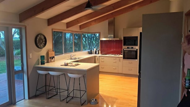 A modern kitchen with a central island, bar stools, a built-in oven, and a large window. - Spacious 5 Bedroom House in Ngāhinapōuri Family Retreat (Ngahinapouri)