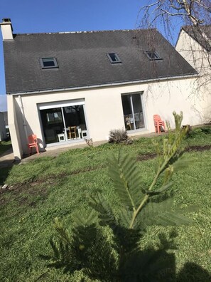 Ein zweistöckiges Haus mit dunklem Dach, großen Fenstern und einer kleinen Veranda.