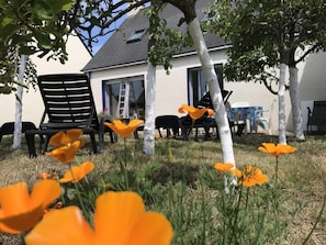 Ein Haus mit weißer Fassade, einem schwarzen Stuhl und orangefarbenen Blumen im Garten.
