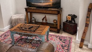 Ein Wohnzimmer mit Fernseher, der 'Welcome' zeigt, einem Holztisch, einem braunen Ledersofa, einem gemusterten Teppich und dekorativen Gegenständen auf einem Holzständer.