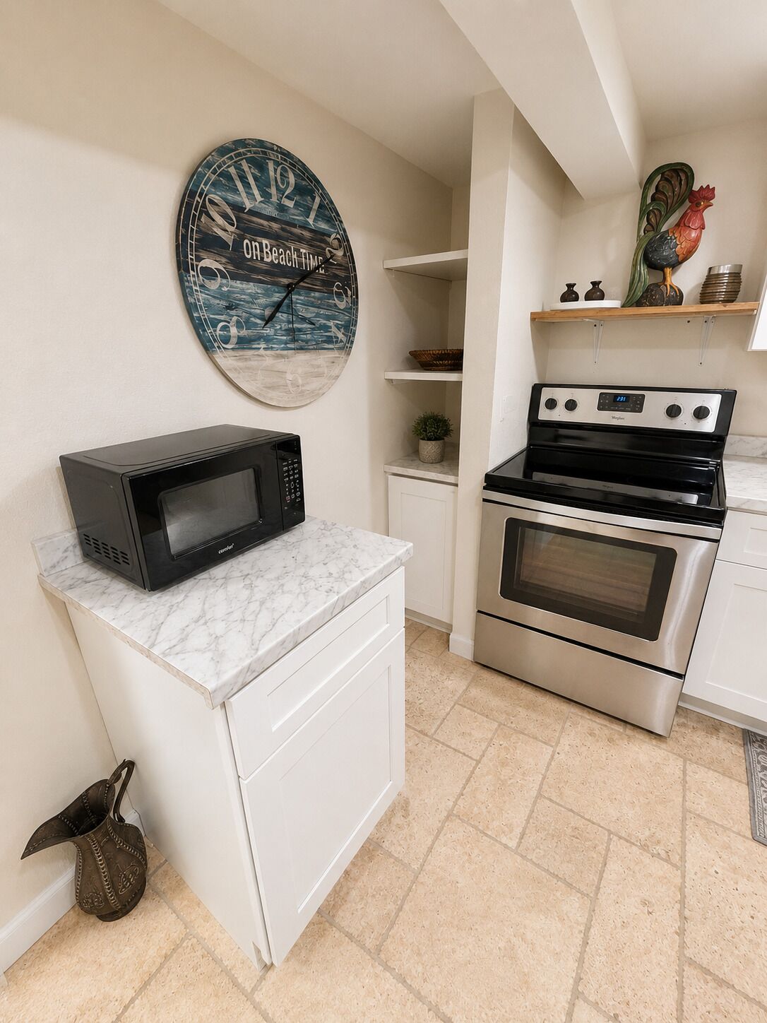 A compact kitchen with a microwave on a marble countertop, a stainless steel oven, and a wall clock.