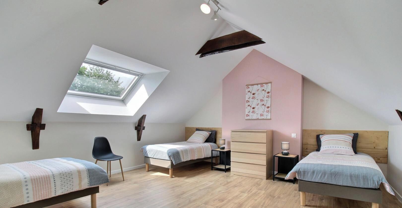 A bedroom with a sloped ceiling, a skylight, two beds, a chair, and a dresser.