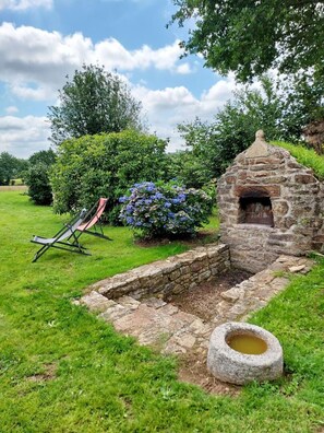 A stone-built outdoor structure with a chimney, a grassy area, and a chair. - De Kerlidec - PLUVIGNER (PLUVIGNER)