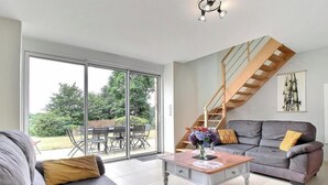 Ein geräumiges Wohnzimmer mit einem grauen Sofa, einem Couchtisch mit einer Vase und einer Treppe, die zu einer oberen Ebene führt.