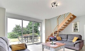 A spacious living room with a grey sofa, a coffee table with a vase, and a staircase leading to an upper level. - De Kerlidec - PLUVIGNER (PLUVIGNER)