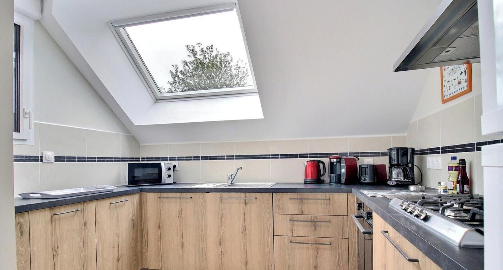Een moderne keuken met dakraam, houten kastjes, een gasfornuis en diverse apparaten.