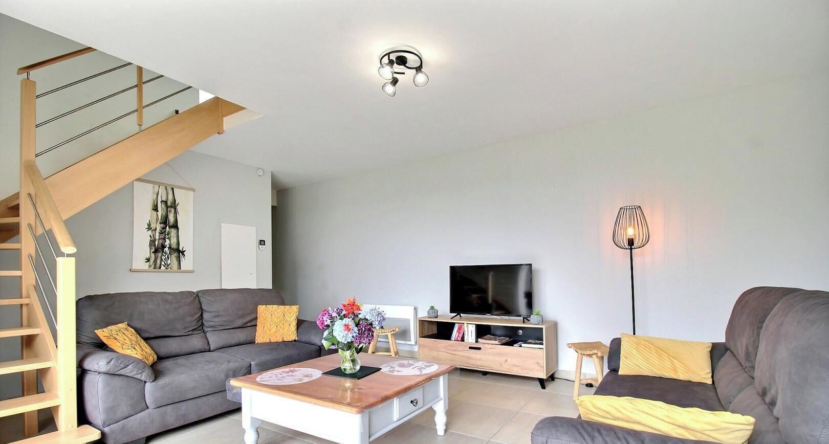 Een moderne woonkamer met een trap, een flatscreen televisie en een salontafel met bloemen.