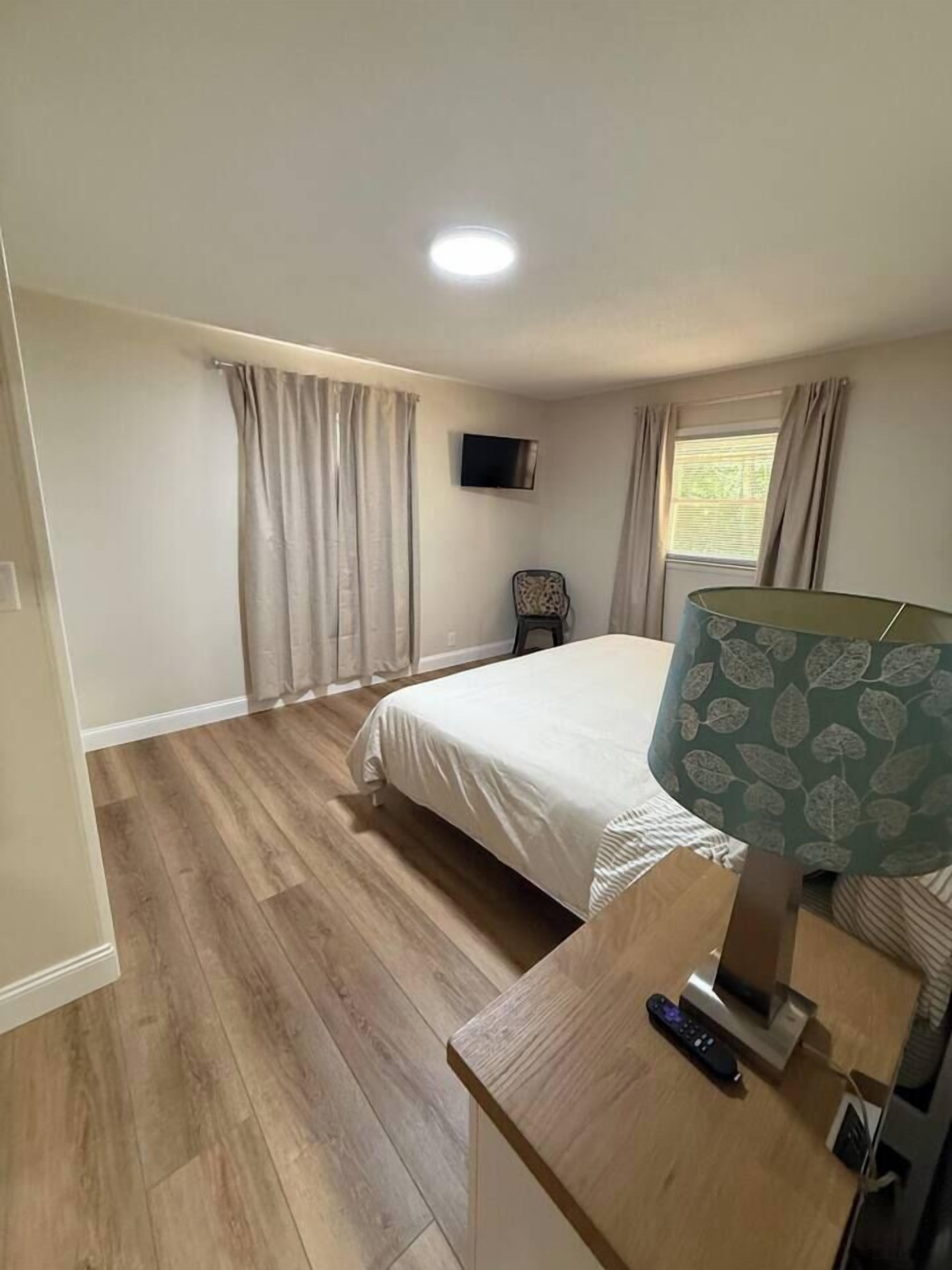A bedroom with a bed, a TV, a lamp, a chair, and a window with curtains.