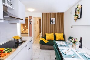 Eine moderne Küche mit Essbereich, ein Bett mit gelben Kissen und ein Esstisch für zwei Personen.