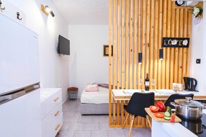 Ein kleines Hotelzimmer mit einer Küchenzeile, einem Bett, einer Essecke und einem an der Wand montierten Fernseher.