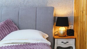 Un letto rifatto con un copriletto e dei cuscini viola, una lampada da comodino e un piccolo comodino in legno con un cassetto.