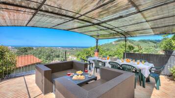 Un patio esterno con una zona salotto riparata, un tavolo da pranzo per due e una vista panoramica sul paesaggio.