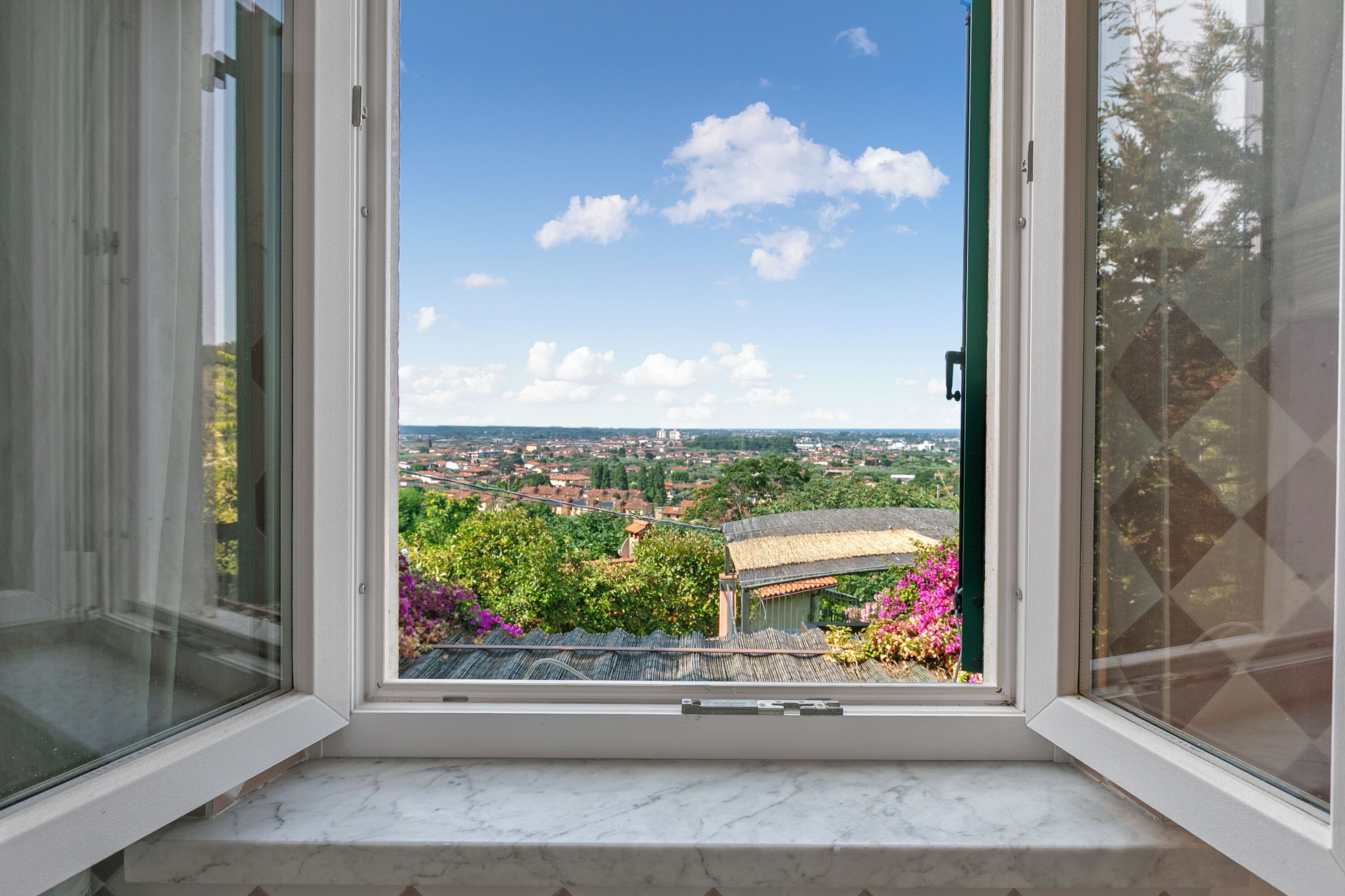 Una finestra con vista sullo skyline cittadino, un balcone e un cielo sereno.