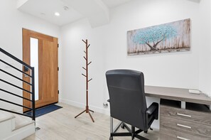 Een moderne kantoorruimte met een houten deur, een kapstok, een bureau met lades en een schilderij van een boom aan de muur.