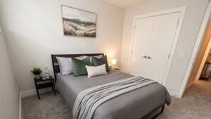 Una camera da letto con un letto, un comodino, una lampada, una porta e un quadro appeso al muro.