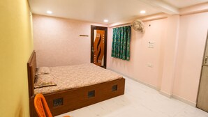 A bedroom with a wooden bed, a single chair, a door, a wall-mounted fan, and a light switch.