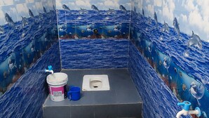 A bathroom with blue tiles, a toilet, a bidet, and a red stool.