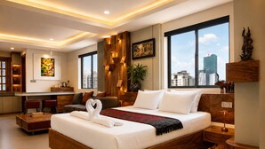 A modern hotel room with a large bed, a sitting area with a sofa and chairs, a kitchen area, and large windows offering a city view. - Dynasty Boutique Hotel (Phnom Penh)