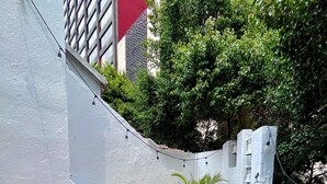 Un pequeño patio exterior con una mesa redonda de vidrio y dos sillas, rodeado de paredes blancas y un suelo rojo.