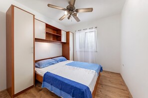 Un dormitorio con cama, armario, ventilador de techo y ventana con cortinas.