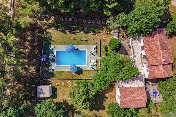 Vista aérea de una propiedad con piscina, rodeada de árboles y una zona vallada.