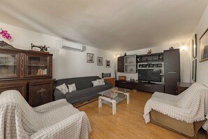 Ein Wohnzimmer mit einer Couch, Sesseln, einem Glastisch, einem Schrank und einem Fernseher.