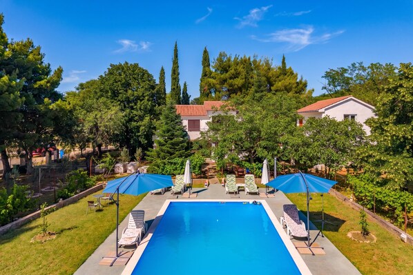 Ein Pool mit Liegestühlen und Sonnenschirmen, umgeben von Bäumen und Gebäuden.