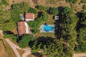 Luftaufnahme eines Grundstücks mit Swimmingpool, umzäunter Garten und einem Gebäude mit rotem Dach.