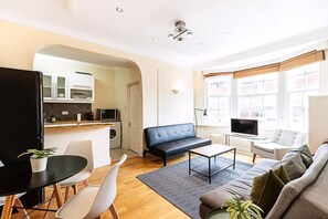Ein modernes Wohnzimmer mit einer Couch, einem Esstisch mit Stühlen, einem Fernseher und einer Küchenzeile mit Schränken und einer Mikrowelle.